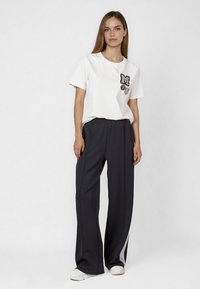 White cotton t-shirt with a decorative "M" and heart patch, paired with dark gray wide-leg pants featuring side stripes and an elastic waistband.