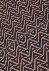 Musterstoff mit einem geometrischen Design aus ineinandergreifenden Dreiecken in Schwarz auf einem gedämpften rosafarbenen Hintergrund, mit ausgefransten Kanten.