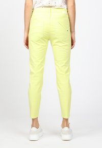 Ljust gula skinny jeans med två bakfickor, minimala sömdetaljer och en slät yta, matchade med vita sneakers.