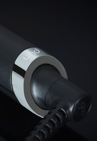 Close-up van een zwarte elektrische stekker die in een apparaat is gestoken met een zilveren ring met het label "ghd" op een donkere achtergrond.
