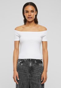 Balta off-the-shoulder krekls ar īsām piedurknēm, pieguļo�šs dizains, mīksta tekstūra, saskaņots ar augsto vidukļa melno uzplēsto džinsu.