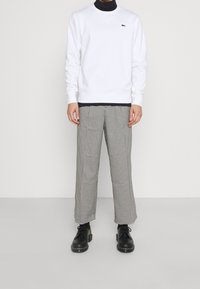 Sudadera blanca de algodón con cuello redondo, combinada con pantalones de patrón de pata de gallo en blanco y negro y zapatos de cordones negros.