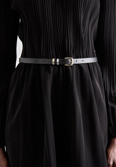 Curea din piele neagră cu un design elegant, având o cataramă din metal aurit și două accente aurii, purtată peste o rochie plisată neagră.