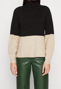 Schwarz-beige Farbblock-Turtleneck-Pullover mit gerippter Textur. Lockerer Schnitt, lange Ärmel und gerader Saum. Tragen mit grünen Lederhosen.