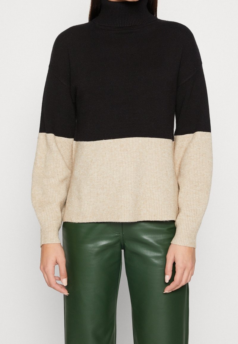 Schwarz-beige Farbblock-Turtleneck-Pullover mit gerippter Textur. Lockerer Schnitt, lange Ärmel und gerader Saum. Tragen mit grünen Lederhosen.