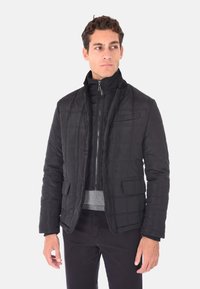 Giubbotto nero trapuntato con colletto alto, zip frontale, due tasche frontali e dettagli grigi in vita. Materiale morbido e leggero.