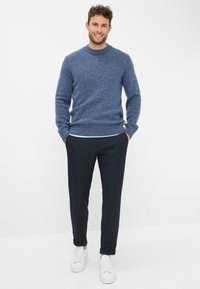 Blauwe gebreide trui met geribde manchetten, gecombineerd met donkere broeken en witte sneakers. Zachte textuur, ronde hals en casual pasvorm.