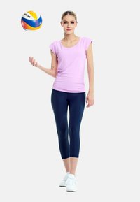 Rosa t-shirt med kort ärm i sportstil, kombinerad med marinblå capribyxor. Vita sneakers. Figuren visas medan den kastar en flerfärgad volleyboll.
