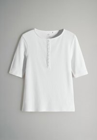 Top bianco a maniche corte in tessuto a coste, con scollatura tonda e patta con sei bottoni sul davanti.