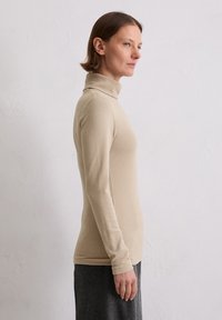 Beige Rollkragenoberteil aus weichem, dehnbarem Stoff. Lange Ärmel, enganliegendes Design, glatte Textur und minimalistisch ohne Muster oder Akzente.