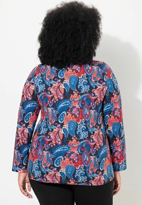 Langärmliges Oberteil mit einem lebhaften Paisley-Muster in Rot, Blau und Weiß auf dunklem Hintergrund. Hergestellt aus dehnbarem Stoff, mit rundem Ausschnitt.