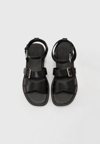Mustad mustad nahk sandaalid kahe ristsanga, reguleeritava pahkluusanga ja nelinurkse varbakuju ning hõbedase pandla aktsendiga.