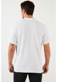 Camisa blanca de manga corta con textura acanalada, que presenta un cuello clásico y un ajuste relajado, mostrada desde atrás con las mangas arremangadas.