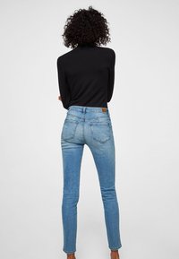 Jeans ajustados en denim azul claro con una cintura de media altura. Presenta bolsillos traseros y una etiqueta de cuero marrón en la cinturilla. Textura suave.