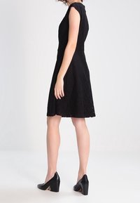 Schwarzes Spitzenkleid mit tailliertem Oberteil, kurzen Ärmeln und schwingendem Rock. Tragen Sie dazu schwarze Heels mit Blockabsatz.