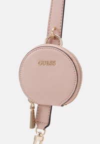 Okrągła różowa torebka z sztucznej skóry z złotymi elementami, zamknięciem na zamek błyskawiczny i paskiem na ramię. Nazwa marki "GUESS" jest wytłoczona z przodu.