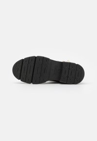 Semelle de chaussure en caoutchouc noir avec un motif texturé, comportant plusieurs rainures et crêtes pour une meilleure adhérence. Design robuste avec un matériau durable.