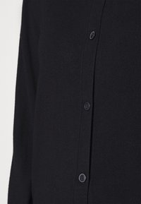 Cardigan negro de punto con cierre de botones en el frente, mangas largas y una textura suave, que destaca un diseño minimalista.