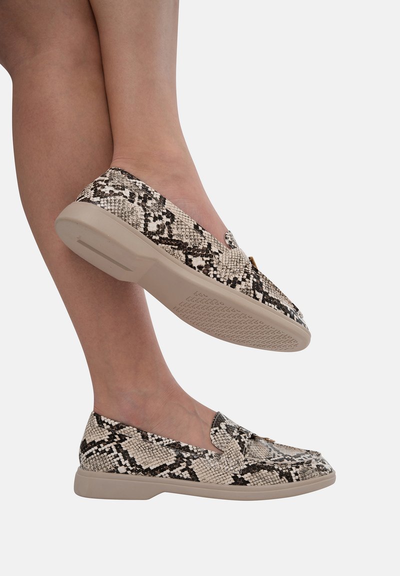 Schoenen met slangenprint zonder veters hebben een textuur in beige en zwart, met een ronde neus en tan rubberen zolen.
