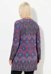 Langermige tuniek in donkergrijs, met een kleurrijk geometrisch patroon met rode, blauwe en witte accenten; zachte textuur en losse pasvorm.