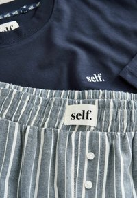Navyblaues Baumwollhemd mit "self."-Logo; blau-weiß gestreifter Rock mit elastischem Bund, Knöpfen und "self."-Label.