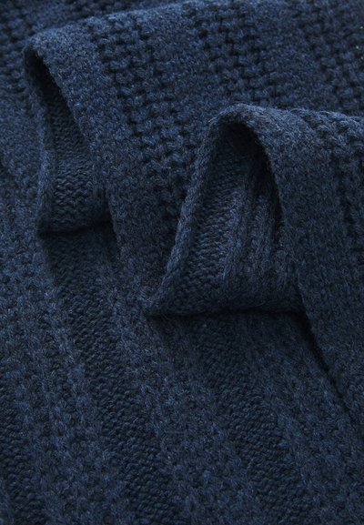 Tissu tricoté bleu marine avec un motif texturé, comportant des rayures en relief. Texture douce et fibreuse avec des détails de couture visibles.