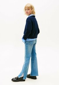 Suéter de punto azul marino superpuesto a una camisa a rayas azul clara, combinado con jeans de campana azul clara y mocasines negros, visto desde atrás.