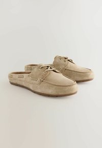 Beige suede slip-on shoes with a rounded toe, lace-up detailing, side vents, and a rubber sole. Smooth texture with minimal accents.