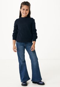 Mörkblå stickad tröja med långa ärmar, tillsammans med utsvängda jeans i denim och svarta glänsande stövlar. Enkel, ren design med subtil textur.