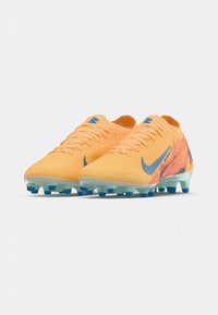 Nike focicipők élénk narancssárga színben, kék kiegészítőkkel; könnyű hálós felsőrész, kontúros forma, és átlátszó talp, tüskékkel.