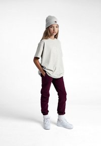 T-shirt oversize gris clair avec un logo rond, pantalon de survêtement bordeaux, baskets blanches et un bonnet côtelé gris clair. Tenue décontractée.