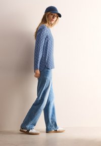 Lysblå mønstrede langærmede bluse parret med højtaljede, brede denimjeans og hvide sneakers, suppleret med en blå kasket.