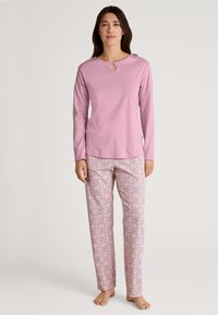 Rooze lange mouwen top met een keyhole halslijn, gecombineerd met gebloemde pyjamabroek in roze en witte kleuren. Zachte stof, relaxte pasvorm.