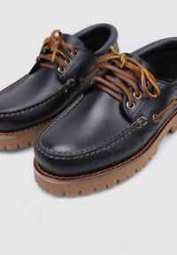 Chaussures en cuir navy avec un design moccasin, lacets marron enfilés dans des œillets dorés, coutures blanches et semelle en caoutchouc marron avec traction.