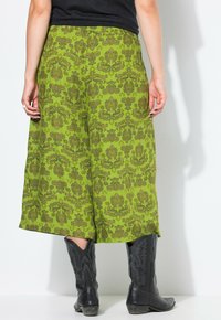Groene culottes met een patroon, gemaakt van textured stof en met een elastische tailleband. Gecombineerd met zwarte cowboylaarzen met decoratieve stiksels.