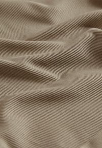 Beige ribota auduma tekstūra ar teksturētu virsmu, kurā redzami maigi salocījumi un maigas viļņus, izceļot tā materiāla un dizaina detaļas.