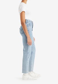 Ljusblå denimjeans med rak passform, hög midja och fransad kant. I kombination med en tajt vit t-shirt och vita sneakers.