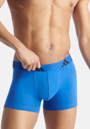 Boxer shorts azules de tela suave, con una cinturilla negra que lleva un logo distintivo, cortados a mitad del muslo con un estilo ajustado.