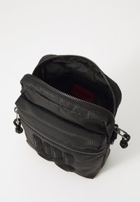 Borsa a tracolla nera con esterno testurizzato, chiusura con zip, tasca anteriore con il bold "HUGO" logo e fodera interna liscia.
