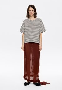 Haut à manches courtes rayé en coton blanc et noir, associé à une jupe longue transparente couleur rouille avec des accents en ruban et des chaussures noires en peluche.