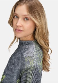 Strickpullover mit hohem Kragen, aus einem strukturierten grauen Stoff mit grünen Akzenten. Das Design betont eine figurbetonte Silhouette und zarte Details.