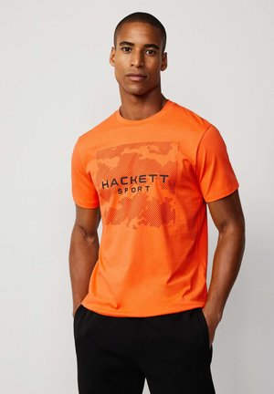 Camiseta de manga corta naranja hecha de algodón, con un estampado gráfico que presenta el texto "HACKETT SPORT" en negro. Textura suave, ajuste casual.