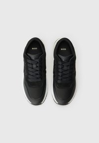 Sneaker nere in pelle liscia e tessuto strutturato, con suola bianca, lacci rotondi e suole interne brandizzate.