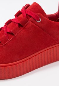 Sneaker en daim rouge avec des lacets ton sur ton et une semelle en caoutchouc épaisse et texturée. Comprend des œillets et un panneau arrière lisse.