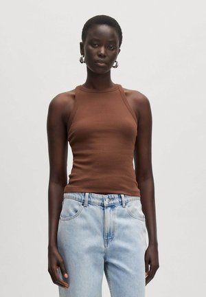 Braunes, geripptes Tanktop mit hohem Kragen, kombiniert mit hellblauen, hoch taillierten Jeans. Das Modell steht vor einem neutralen Hintergrund.