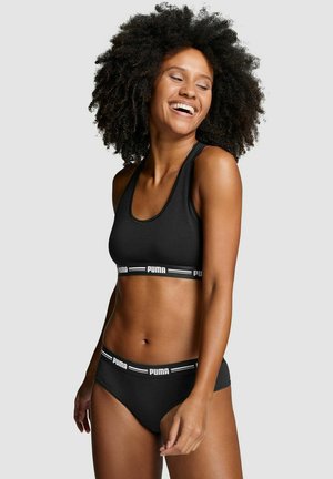 Schwarzes Sport-BH- und Bikini-Set mit einem kontrastierenden weißen Puma-Logo-Band. Geschmeidige Textur, enganliegende Form und minimalistisches Design.