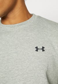 Light grey short-sleeve t-shirt made of soft fabric, featuring a black Under Armour logo on the chest and a classic crew neckline.
