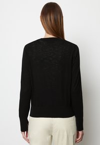 Czarny sweter z długim rękawem o okrągłym dekolcie, z teksturowanym wzorem dzianiny i ściągaczami na mankietach, noszony na jasnych spodniach.
