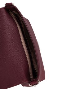Burgundská texturovaná kožená kabelka se zipem, otevřená, aby odhalila hladký béžový interiér a dvě oddělení. Přítomné stříbrné kovové doplňky.