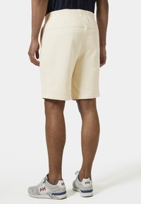 Beige shorts met een elastische tailleband, zijzakken en een relaxte pasvorm, gecombineerd met grijze sneakers met blauwe en witte accenten.